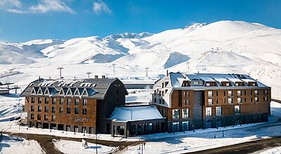 Hotelbau aus dunklem Holz in verschneiter Berglandschaft