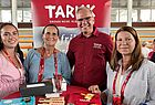 Drei Männer und eine Frau auf einer Reisemesse lächeln für ein Foto in die Kamera