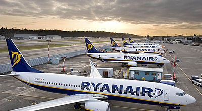 Mehrere weiß-blaue Flugzeuge des Billigfliegers Ryanair stehen nebeneinander auf dem Vorfeld eines Flughafens vor einem dramatischen Abendhimmel