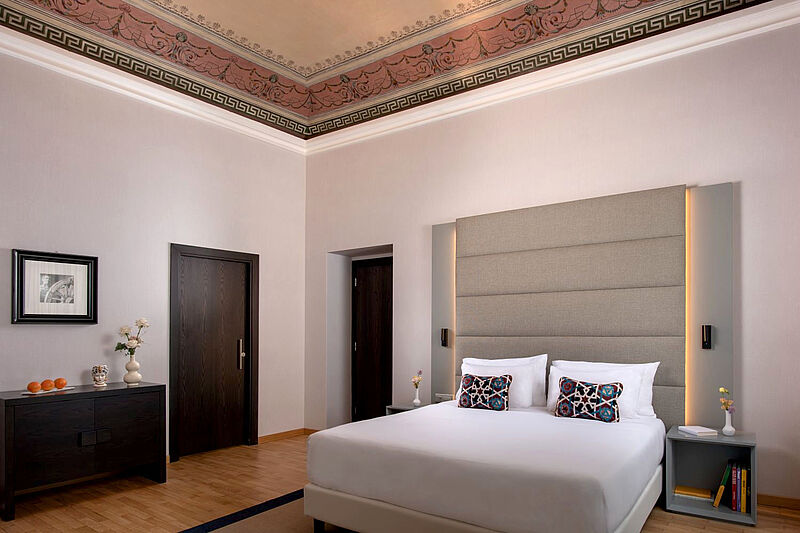 Modern eingerichtetes Hotelzimmer in einem italienischen Palazzo mit reich verzierter Decke.