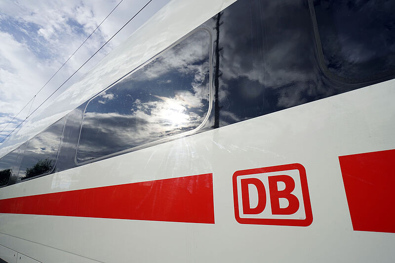 Ein ICE-Schnellzug der Deutschen Bahn in rot-weißer Lackierung in Nahaufnahme. Sonne und Himmel werden in einem Fenster reflektiert.