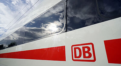 Ein ICE-Schnellzug der Deutschen Bahn in rot-weißer Lackierung in Nahaufnahme. Sonne und Himmel werden in einem Fenster reflektiert.