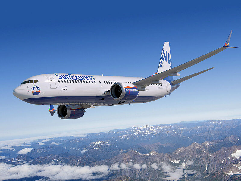 Türkei-Flieger Sun Express baut auch Deutschland-Strecken weiter aus. Foto: Sun Express Ein Flugzeug der Airline Sun Express mit weiß-blauer Lackierung fliegt bei sonnigem Wetter über Wolken und eine Gebirgslandschaft hinweg