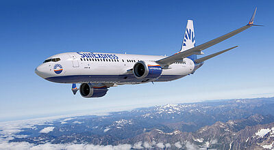 Ein Flugzeug der Airline Sun Express mit weiß-blauer Lackierung fliegt bei sonnigem Wetter über Wolken und eine Gebirgslandschaft hinweg