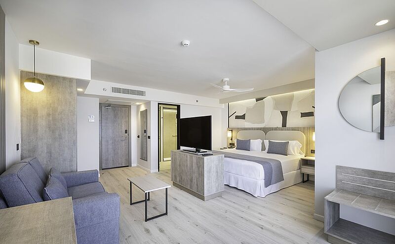 Modernes und helles Hotelzimmer mit Kingsize-Bett, Sofa, Flachbild-TV und stilvollem Interieur in neutralen Farben – ideal für komfortablen Aufenthalt im Urlaub oder Business-Trip.