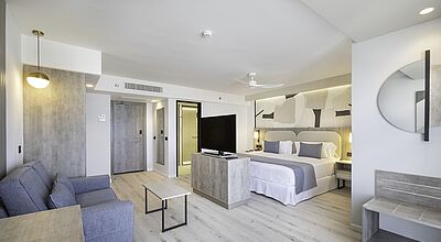 Modernes und helles Hotelzimmer mit Kingsize-Bett, Sofa, Flachbild-TV und stilvollem Interieur in neutralen Farben – ideal für komfortablen Aufenthalt im Urlaub oder Business-Trip.