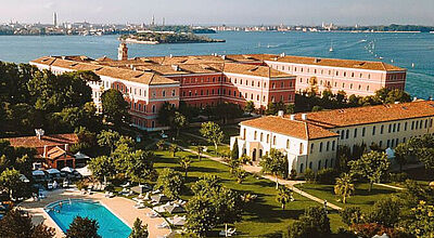 Das San Clemente Palace in Venedig wird nun von Mandarin Oriental geführt. Foto: Mandarin Oriental Luftaufnahme des luxuriösen San Clemente Palace Hotels auf der privaten Insel San Clemente in Venedig mit Blick auf die Altstadt, gepflegten Gärten, Poolbereich und historischen Gebäuden – ehemals Kempinski, künftig Mandarin Oriental.