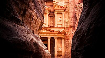 Blick durch eine Felsspalte auf einen antiken Grabtempel im jordanischen Petra, der in einen Felsen geschlagen wurde.