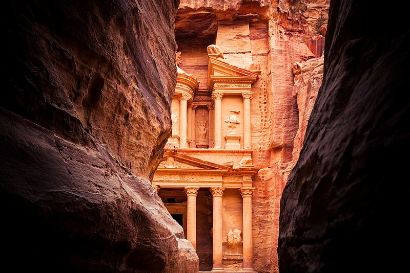 Blick durch eine Felsspalte auf einen antiken Grabtempel im jordanischen Petra, der in einen Felsen geschlagen wurde.