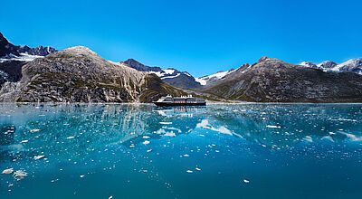 Ein Kreuzfahrtschiff mit dunklem Rumpf und weißem Aufbau passiert in Alaska gewaltige Gletscher.