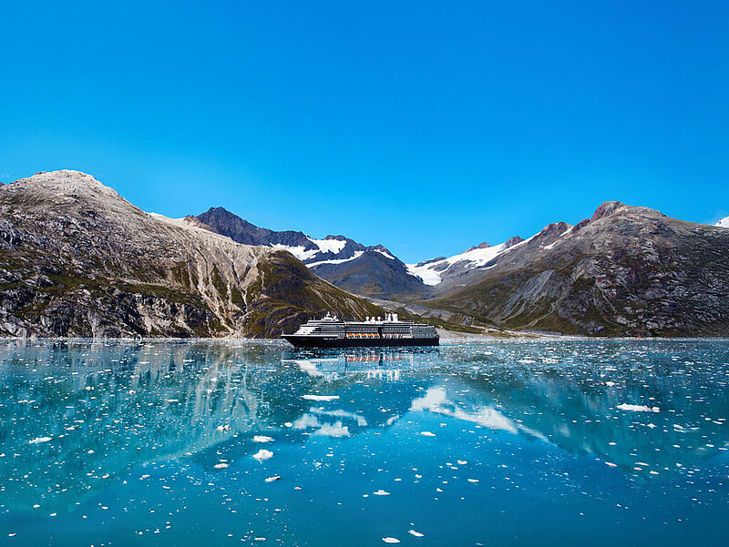 Ein Kreuzfahrtschiff mit dunklem Rumpf und weißem Aufbau passiert in Alaska gewaltige Gletscher.