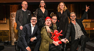 Sieben lachende Menschen mit Statue eines roten Löwen