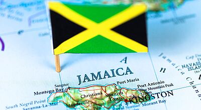 Jamaika auf der Landkarte mit Fähnchen in den Nationalfarben Schwarz, Grün und Gelb – symbolisch für beliebte Reiseziele wie Montego Bay, Kingston und die Blue Mountains. 