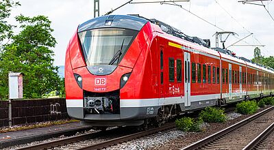 Der Bahnverkehr in Stuttgart soll durch das Projekt Stuttgart 21 digitaler und effizienter werden – doch es drohen Verzögerungen. Ein roter Personenzug fährt auf Bahngleisen durch eine Landschaft.