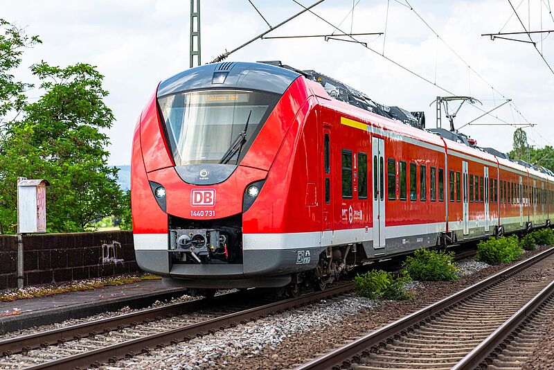 Ein roter Personenzug fährt auf Bahngleisen durch eine Landschaft.