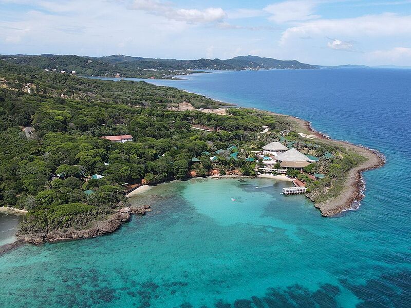 Das Sol Roatan Media Luna Resort liegt an der Südküste der Karibikinsel Roatan. Foto: Melia Hotels International Luftaufnahme der tropischen Insel Roatan in Honduras mit üppigem Regenwald, türkisblauem Karibikmeer und einem idyllisch gelegenen Strandresort – beliebtes Reiseziel für Taucher und Badeurlauber in Mittelamerika.