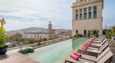 Eine Dachterrasse mit einem Infinitypool, dahinter sieht man Häuser
