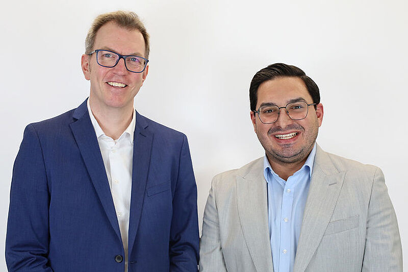 Zwei Manager in Hemd und Jackett stehen lächelnd nebeneinander