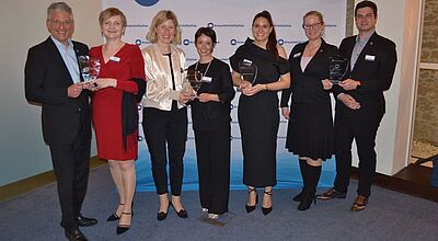 Die Sieger der Fair Play Awards (von links): Timo Weißenstein und Melanie Marra (Aida), Stefanie Vollmuth und Andrea Hendel(Ponant), Isabella Miller (Nicko) sowie Eva Arning und Paul Schnitzer (Port of Kiel). Foto: ck Fünf Frauen und zwei Männer posieren bei einer Preisverleihung mit Awards vor einer Fotowand.