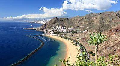 Die Anex-Gruppe präsentiert auf ihrer Roadshow das Winterprogramm 2025, darunter beliebte Ziele wie die Kanaren (im Bild Teneriffa Luftaufnahme des gebogenen Sandstrands Playa de las Teresitas mit Wellenbrecher, türkisblauem Wasser und Bergkulisse von Teneriffa