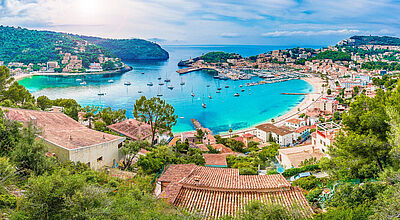 Panoramablick auf die Bucht von Port de Soller mit türkisblauem Wasser, Segelbooten im Hafen und mediterranen Häusern an den Berghängen