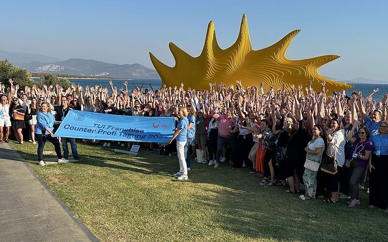 Gruppe von Reiseverkäufern auf einer Wiese vor einer Sonnenskulptur