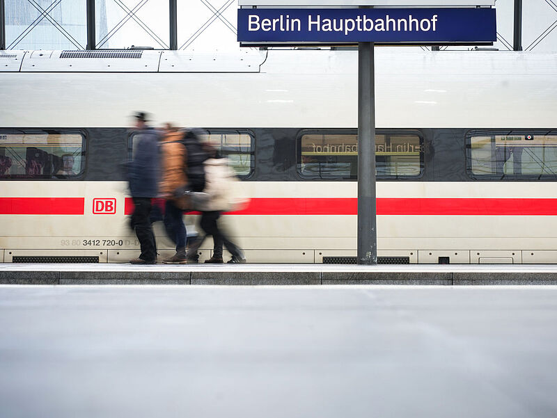 ICE-Zug am Gleis im Berliner Hauptbahnhof, davor unscharf Bahnreisende.