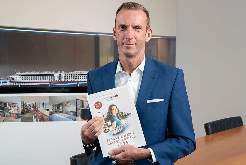 Arosa-Vertriebschef Stefan Sprunk mit Kreuzfahrtkatalog im Büro