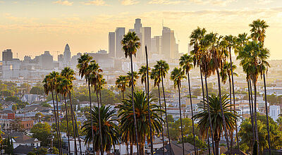 Die Trump-Regierung streicht der Marketing-Organisation Brand USA das Budget radikal zusammen. Das könnte im Vorfeld der Fußball-WM und der Olympischen Spiele in Los Angeles (Bild) noch zum Problem werden Los Angeles Skyline bei Sonnenuntergang, Wolkenkratzer der Innenstadt hinter Palmen und Wohngebieten im Vordergrund.