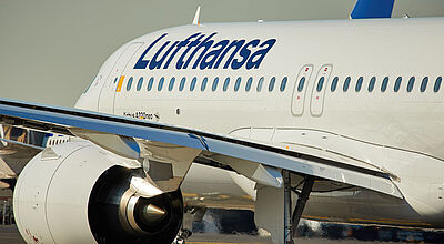 Flugzeugrumpf und ein Triebwerk eines Airbus A 320 von Lufthansa, der über eine Start- und Landebahn rollt, in Nahaufnahme von schräg hinten.
