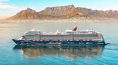 Auch Kapstadt findet sich im neuen Winterprogramm Ein Kreuzfahrtschiff mit dunkelblauem Rumpf fährt bei schönem Wetter vor der Kulisse Kapstadts. Unter blauem Himmel thront der Tafelberg