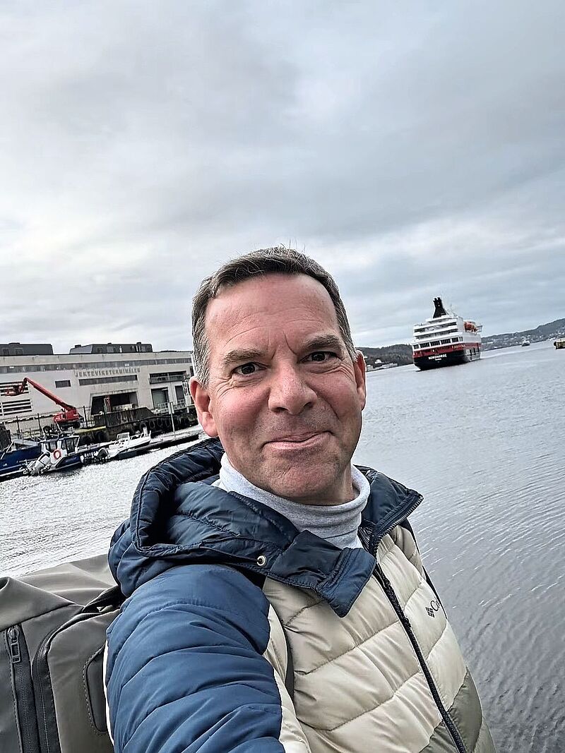 Frank Wegener, Sales-Manager von Hurtigruten, vor einem Kreuzfahrtschiff in einem norwegischen Hafen – Porträtfoto 