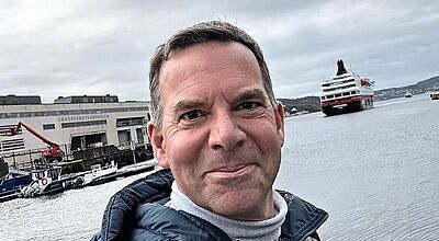 Frank Wegener, Sales-Manager von Hurtigruten, vor einem Kreuzfahrtschiff in einem norwegischen Hafen – Porträtfoto 