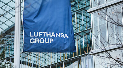 Eine blaue Fahne der Lufthansa Group weht vor der Glasfront der Konzernzentrale