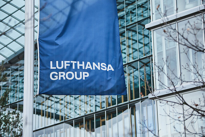Eine blaue Fahne der Lufthansa Group weht vor der Glasfront der Konzernzentrale