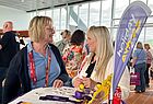Zwei Frauen im Gespräch. Im Raum sind viele andere Menschen. Die beiden stehen vor einem Tisch, auf dem auch ein Holiday Extras Aufsteller steht
