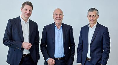 Drei Männer im Anzug stehen vor einer Wand