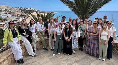 Gruppenfoto der TTS Young Stars 2025 auf Fuerteventura mit Blick auf die Playa de Jandia – junge Touristikerinnen und Touristiker beim Branchennachwuchs-Event vor malerischer Kulisse mit Palmen, Sandstrand und türkisblauem Atlantik.