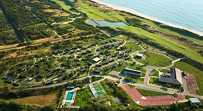 Luftaufnahme eines modernen Ferienresorts an der Atlantikküste mit Ferienhäusern im Grünen und Poolanlage, Tennisplatz, Sport- und Freizeitbereichen sowie angrenzendem Golfplatz direkt am Sandstrand