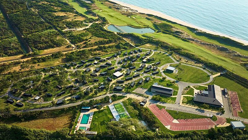Luftaufnahme eines modernen Ferienresorts an der Atlantikküste mit Ferienhäusern im Grünen und Poolanlage, Tennisplatz, Sport- und Freizeitbereichen sowie angrenzendem Golfplatz direkt am Sandstrand
