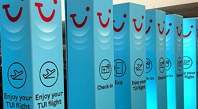 Blaue Stelen mit TUI Logo und Check-in-Symbolen