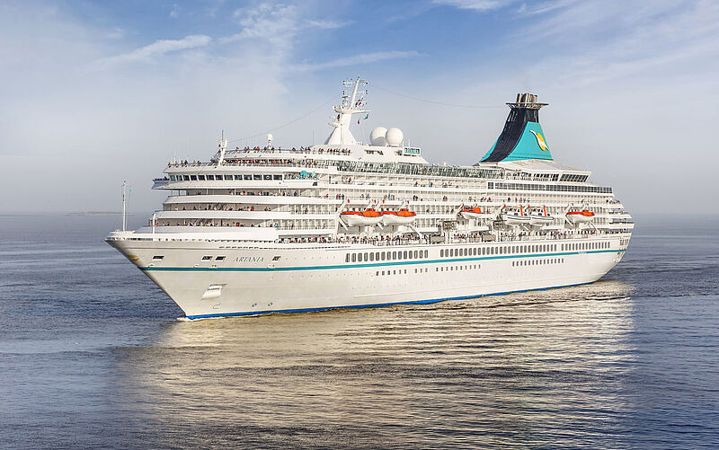 Ein Kreuzfahrtschiff mit weißem und türkisfarbenem Anstrich fährt auf offener See.