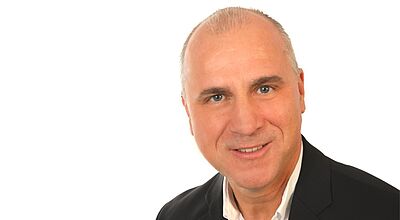 Spätestens zum 1. Juni 2026 soll Dennis Schrahe Hauptgeschäftsführer von Alltours Flugreisen, Byebye sowie von Reisecenter Alltours werden. Porträt eines Mannes mittleren Alters, der in die Kamera lächelt. Er trägt ein weißes Hemd unter einer grauen Anzugjacke
