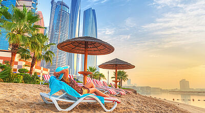 Sandstrand vor Hochhauskulisse mit Liegestühlen und Strohschirmen vor imposanter im goldenen Sonnenuntergang