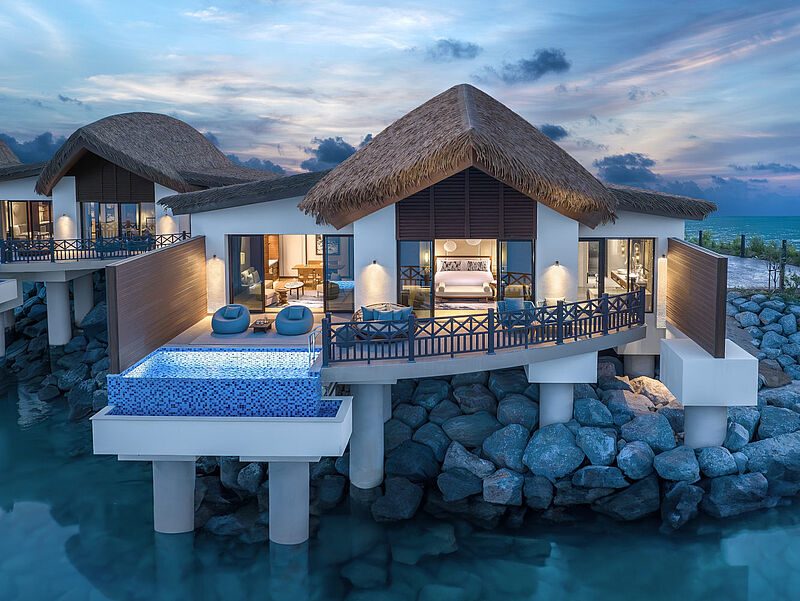 Luxuriöse Overwater-Villa mit Pool und Strohdach auf Stelzen über türkisfarbenen Meer bei Sonnenuntergang