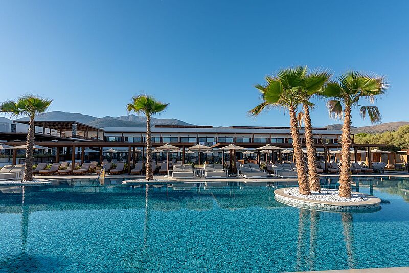 Alltours hat das Allsun Hotel Carolina Sun Beach soft auf Kreta eröffnet Blick über einen blauen Swimmingpool auf ein dreistöckiges Hotelgebäude, dahinter ein blauer Abendhimmel