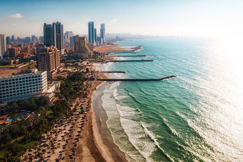 Luftaufnahme einer Küstenstadt mit Wolkenkratzern, Sandstrand und türkisfarbenem Meer mit Wellenbrechern