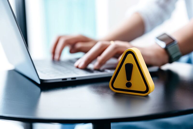 Hände gleiten über eine Laptop-Tastatur, es ist ein Warnzeichen zu sehen