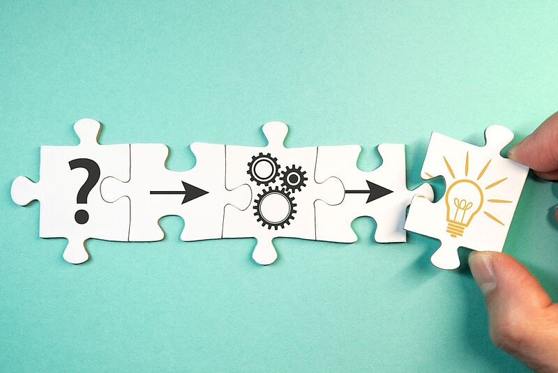 Bei der Mitgliederversammlung des VUSR in Düsseldorf geht es auch um eine Neuausrichtung und die Zukunft des Verbandes Vier zusammengefügte Puzzleteile auf türkisem Hintergrund zeigen eine Abfolge: ein Fragezeichen, einen Pfeil, Zahnräder, einen weiteren Pfeil und am Ende eine Hand, die das letzte Puzzleteil mit einer leuchtenden Glühbirne einsetzt – sinnbildlich für den Weg von der Frage über den Prozess zur Idee oder Lösung.