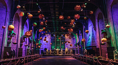 Eine dunkle halle mit bunten Lichtelementen und von der Decke hängenden künstlichen Kürbissen.